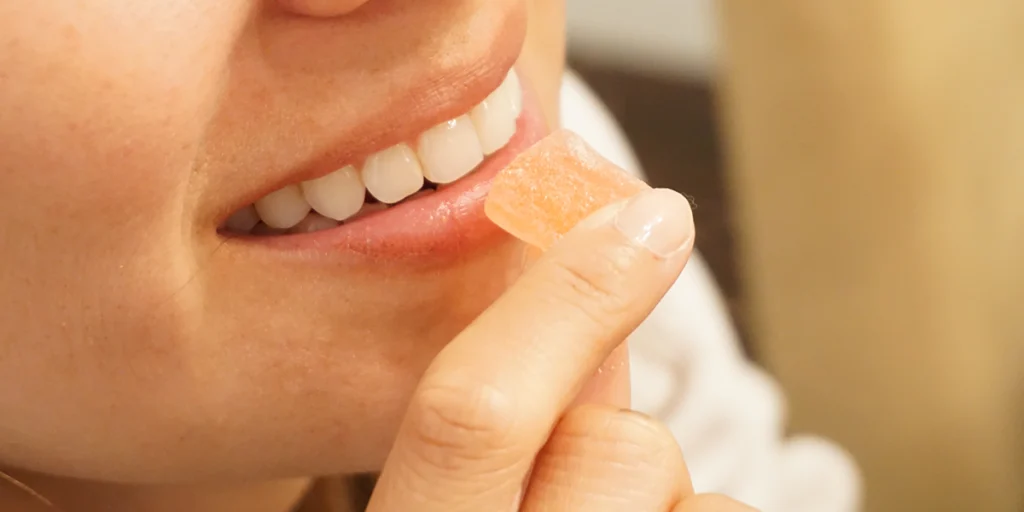 Close-up of a smiling person holding an edible cannabis gummy between their fingers near their mouth, with a warm, relaxed mood.